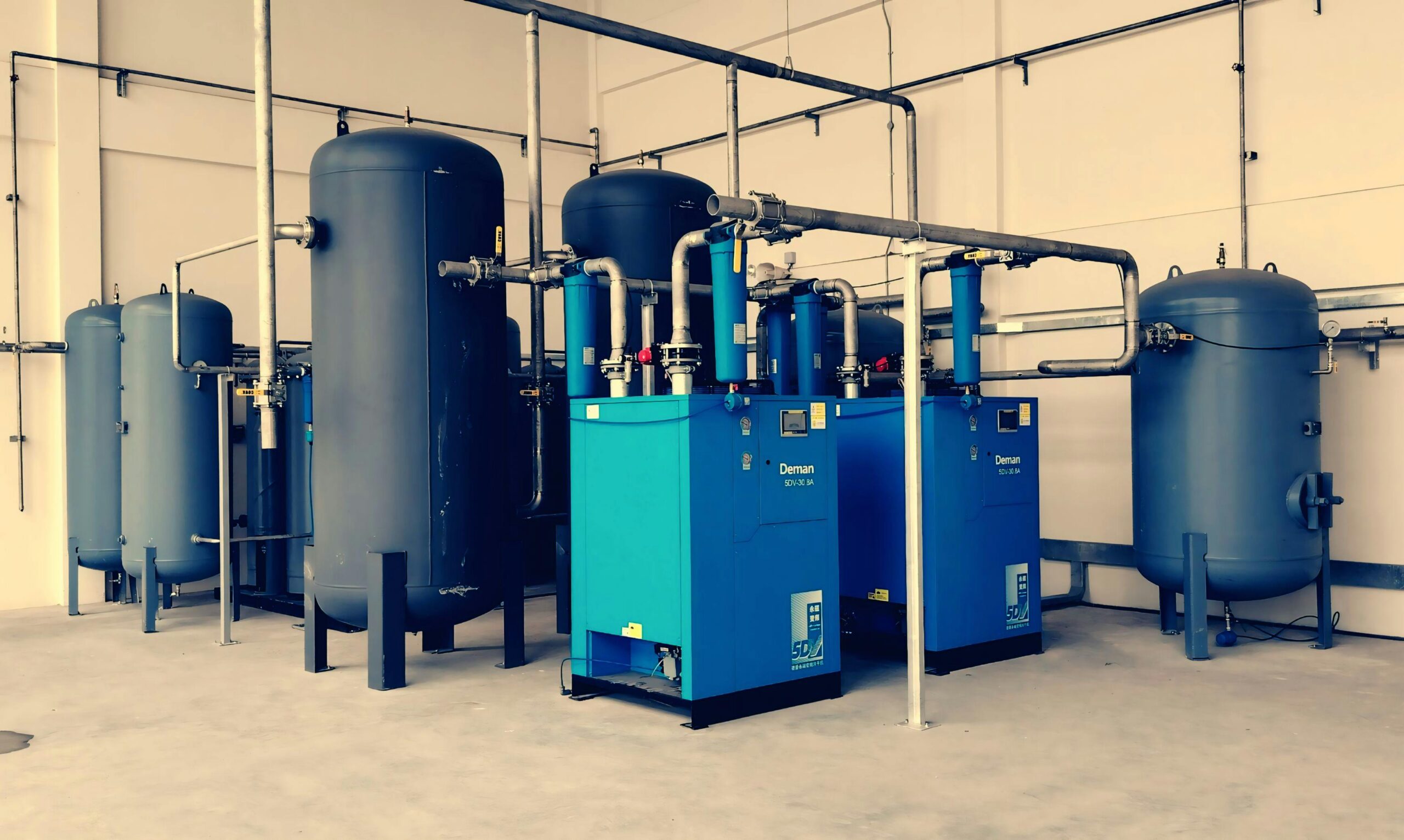 Industrial air compressor setup with blue tanks and pipes inside a plant.
